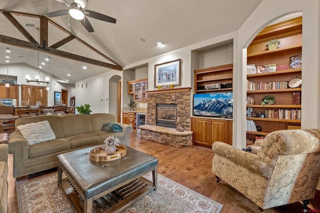 living room featuring light wood-type flooring, visible vents, built in shelves, arched walkways, and a stone fireplace