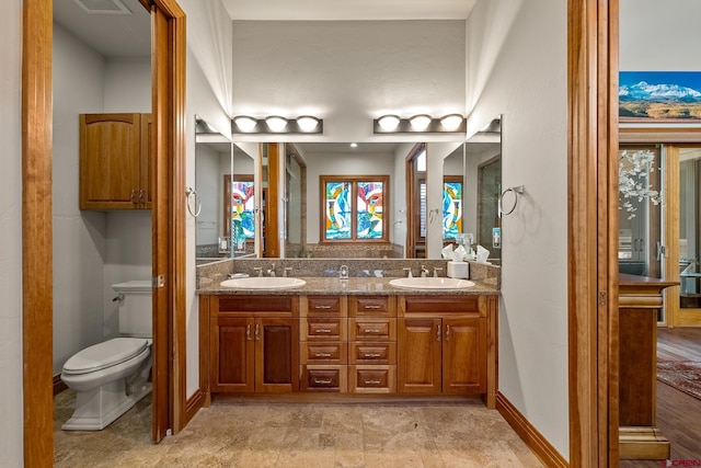 bathroom with double vanity, toilet, baseboards, and a sink