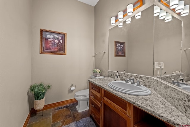 bathroom with vanity, stone tile floors, toilet, and baseboards