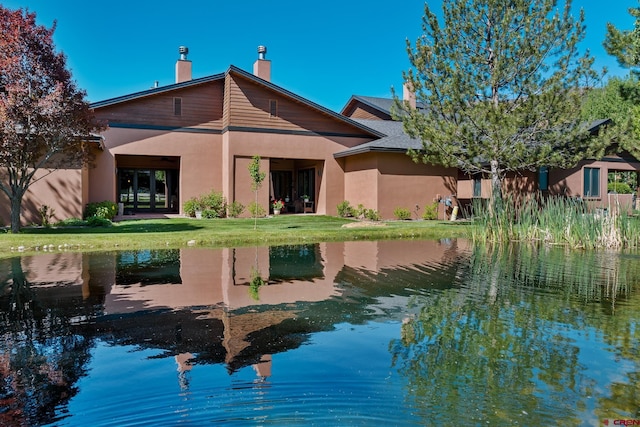 back of house with a water view, a lawn, and a chimney