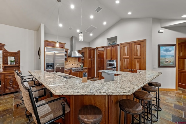 kitchen featuring a sink, stone tile floors, appliances with stainless steel finishes, a breakfast bar area, and wall chimney exhaust hood