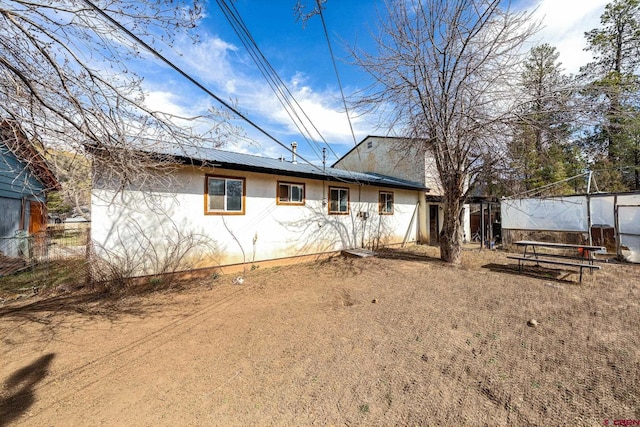 rear view of house with metal roof, fence, and stucco siding