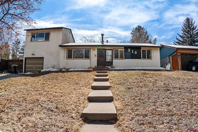 tri-level home with stucco siding, fence, an outdoor structure, an attached garage, and metal roof