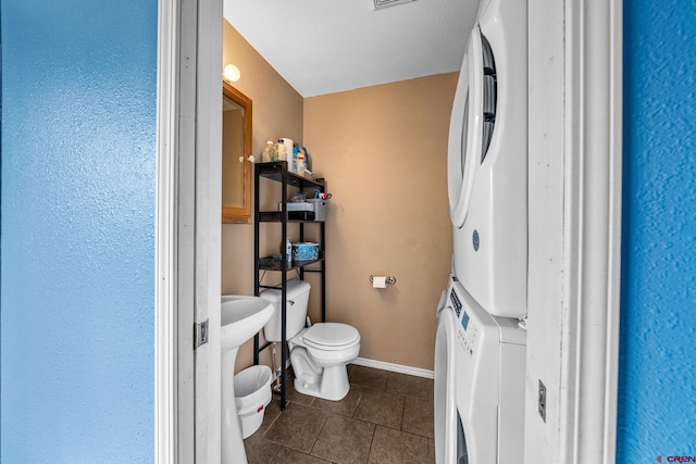 half bath featuring visible vents, baseboards, tile patterned floors, stacked washer / dryer, and toilet