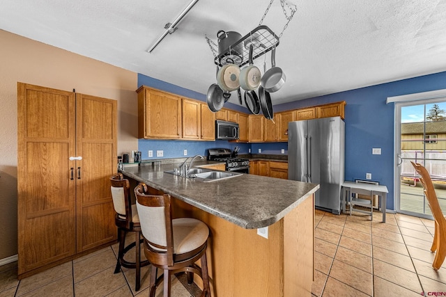 kitchen featuring a sink, stainless steel appliances, dark countertops, and brown cabinetry