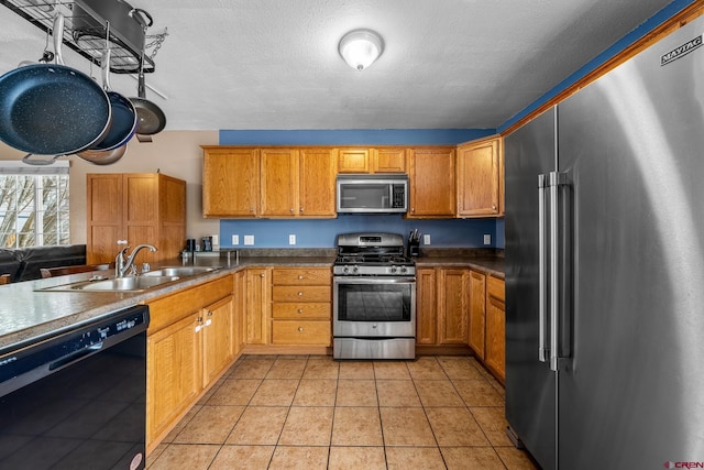 kitchen featuring brown cabinetry, light tile patterned flooring, a sink, appliances with stainless steel finishes, and a textured ceiling