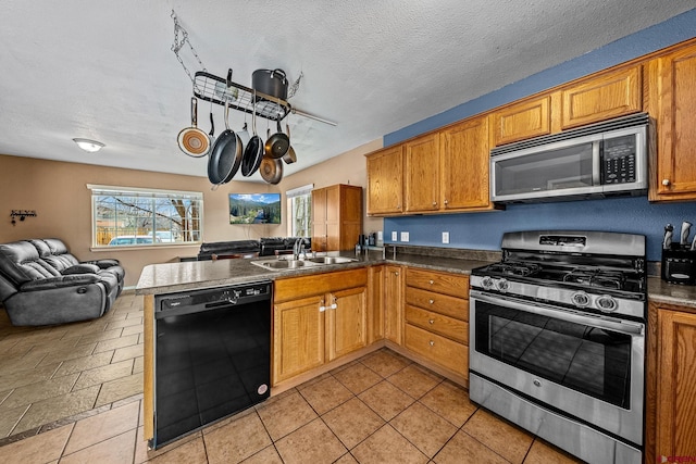 kitchen with a peninsula, a sink, open floor plan, appliances with stainless steel finishes, and brown cabinets