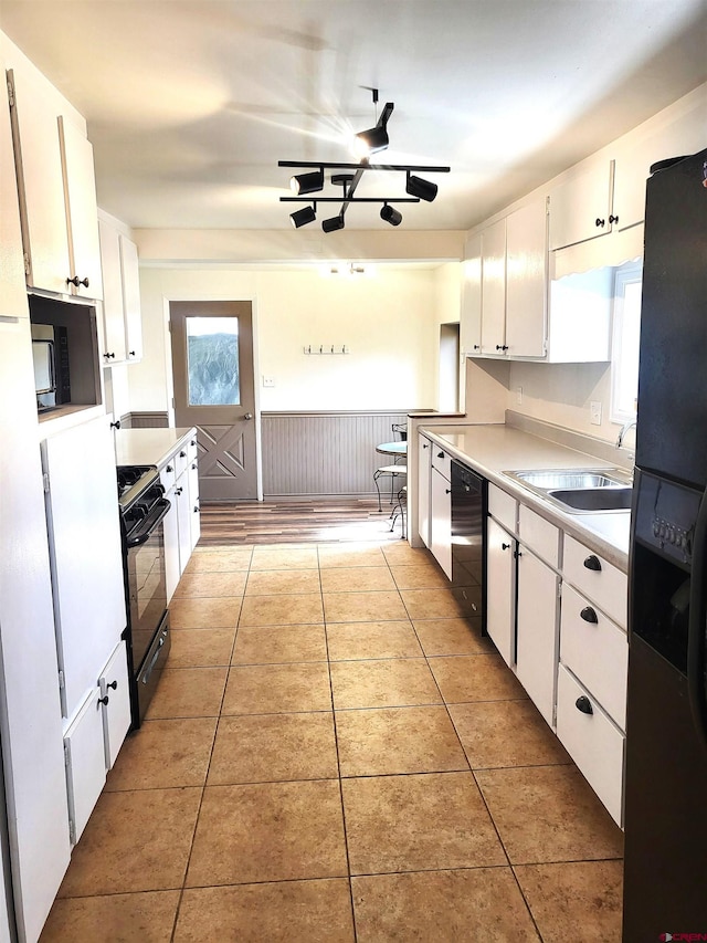 kitchen with a sink, black appliances, light tile patterned flooring, and light countertops