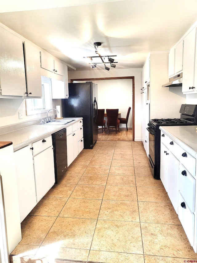 kitchen with black appliances, under cabinet range hood, a sink, light tile patterned flooring, and white cabinets