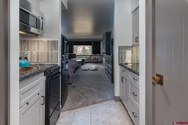 kitchen featuring backsplash, stainless steel microwave, light colored carpet, and black electric range