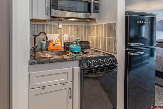 kitchen featuring black appliances, a sink, dark countertops, tasteful backsplash, and white cabinetry