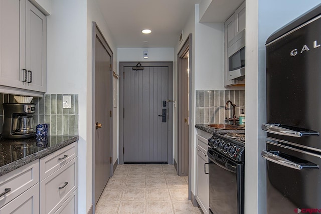 kitchen featuring black electric range, a sink, stainless steel microwave, fridge, and light tile patterned floors