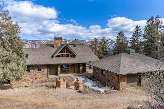 view of front of home featuring a shingled roof, a garage, stone siding, and a chimney