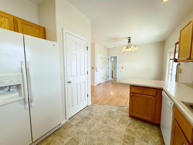 kitchen with white appliances, a peninsula, a chandelier, and brown cabinetry