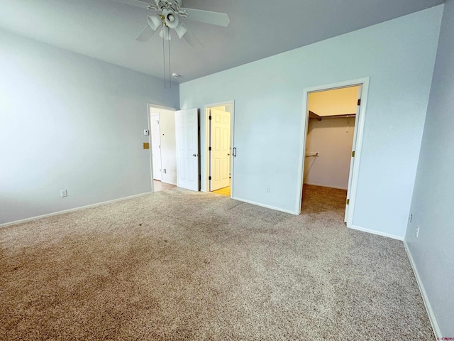 unfurnished bedroom featuring a walk in closet, carpet flooring, baseboards, and ceiling fan