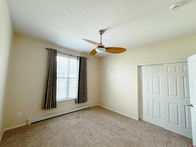 unfurnished bedroom with a baseboard heating unit, carpet, a closet, and a ceiling fan