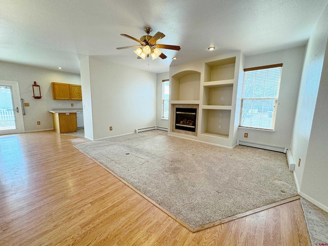 unfurnished living room with light wood finished floors, plenty of natural light, built in shelves, and a baseboard heating unit