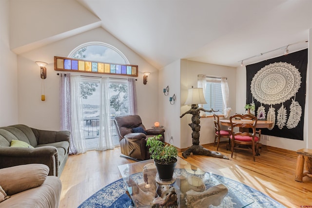 living area with vaulted ceiling, wood finished floors, baseboards, and track lighting