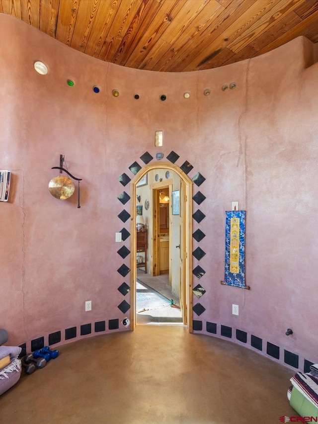 misc room featuring arched walkways, wood ceiling, and finished concrete flooring