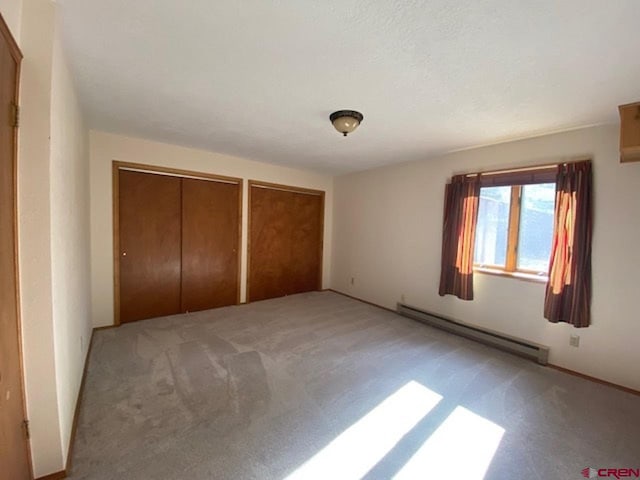 unfurnished bedroom with baseboard heating, light colored carpet, and multiple closets