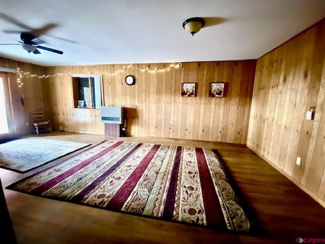 interior space with wooden walls, wood finished floors, and a ceiling fan