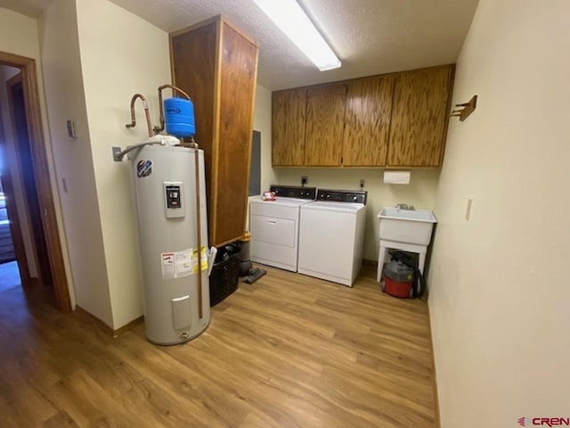 laundry room with baseboards, water heater, a textured ceiling, light wood-type flooring, and washer and clothes dryer