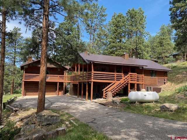 log home with a garage, a wooden deck, concrete driveway, and a chimney