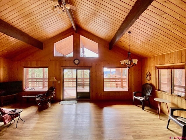 living area with wooden walls, ceiling fan with notable chandelier, vaulted ceiling with beams, and wood finished floors