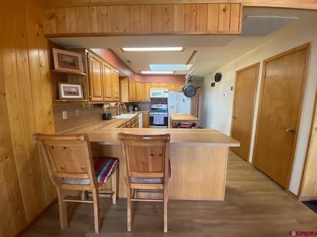 kitchen featuring light wood-type flooring, a sink, white appliances, a peninsula, and light countertops