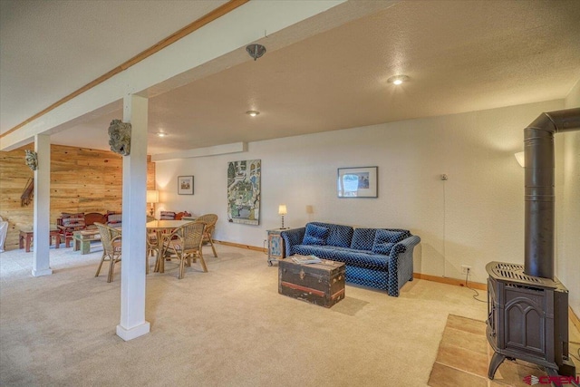 living area featuring wooden walls, light colored carpet, a wood stove, and baseboards