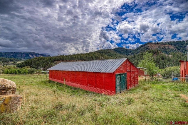 view of outbuilding with a mountain view, an outdoor structure, a wooded view, and fence