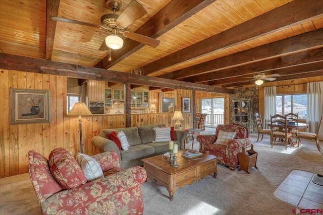 carpeted living room featuring beamed ceiling, a healthy amount of sunlight, ceiling fan, and wood walls