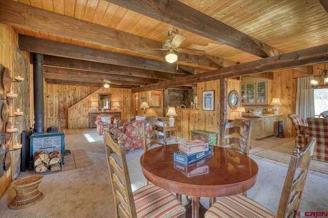 dining space featuring wooden walls, beamed ceiling, a wood stove, and ceiling fan