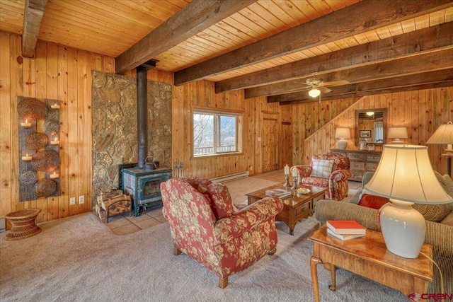 carpeted living room featuring beam ceiling, a wood stove, wood walls, a baseboard heating unit, and wooden ceiling