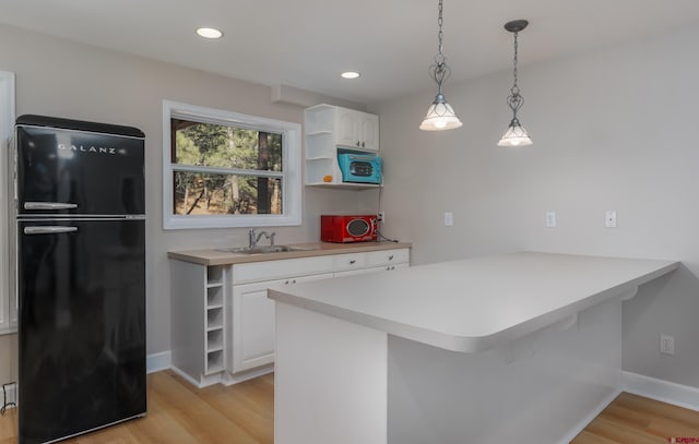 kitchen featuring open shelves, a peninsula, freestanding refrigerator, and a sink