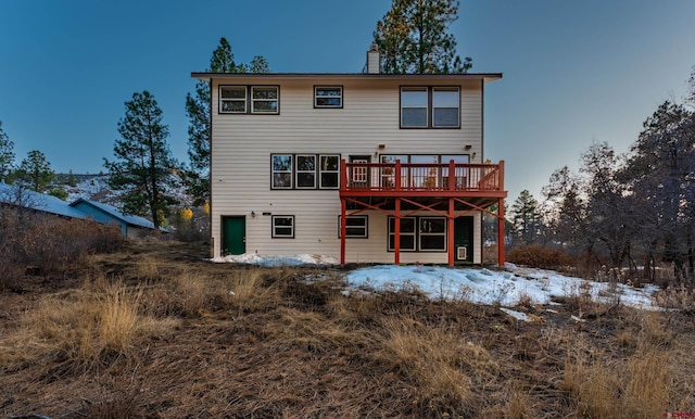 snow covered back of property with a wooden deck and a chimney