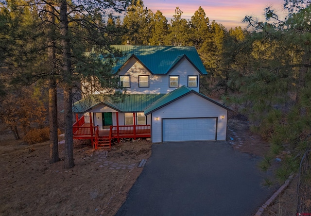 chalet / cabin with a porch, driveway, metal roof, and an attached garage