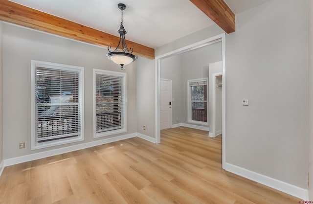 unfurnished dining area featuring beamed ceiling, baseboards, and light wood-style floors