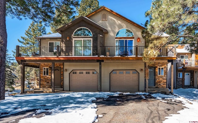 rustic home featuring stone siding, a balcony, driveway, and a garage