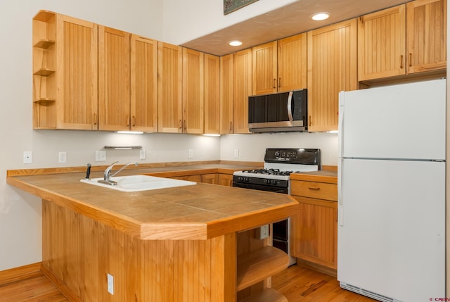 kitchen featuring open shelves, stainless steel microwave, a sink, freestanding refrigerator, and gas range