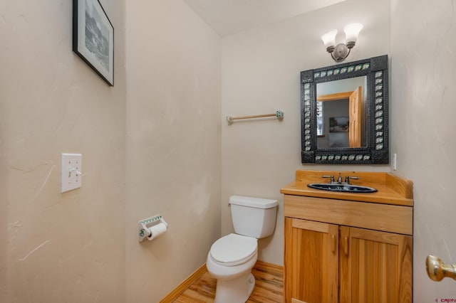 half bathroom with baseboards, toilet, wood finished floors, and vanity