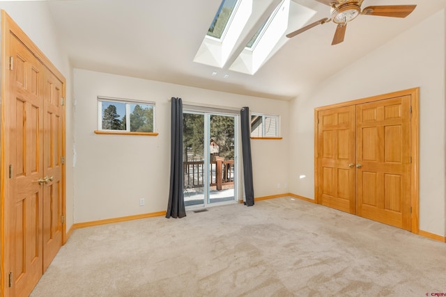 unfurnished bedroom with access to exterior, carpet flooring, lofted ceiling with skylight, and baseboards