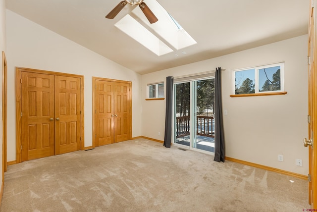 unfurnished bedroom with lofted ceiling with skylight, two closets, access to outside, carpet flooring, and baseboards