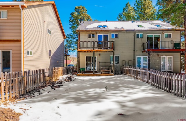 snow covered house featuring french doors, a balcony, and a fenced backyard