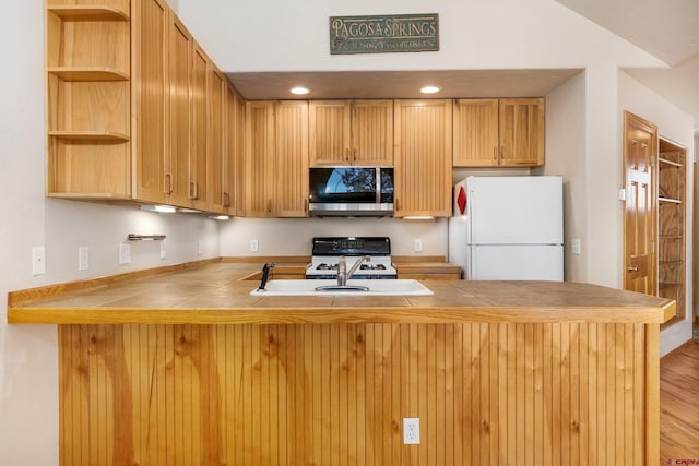 kitchen with white appliances, tile counters, a peninsula, and a sink