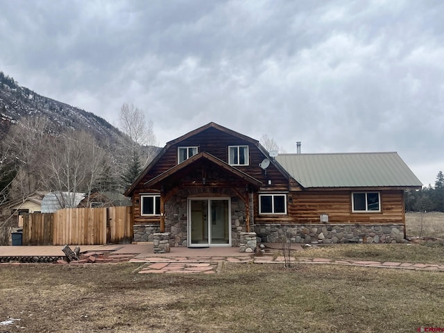 rear view of property with a patio, fence, stone siding, a mountain view, and metal roof