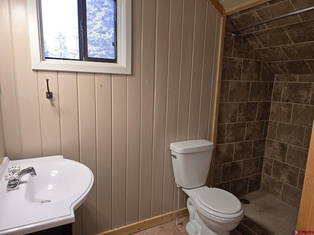 bathroom featuring a sink, wooden walls, toilet, and tiled shower