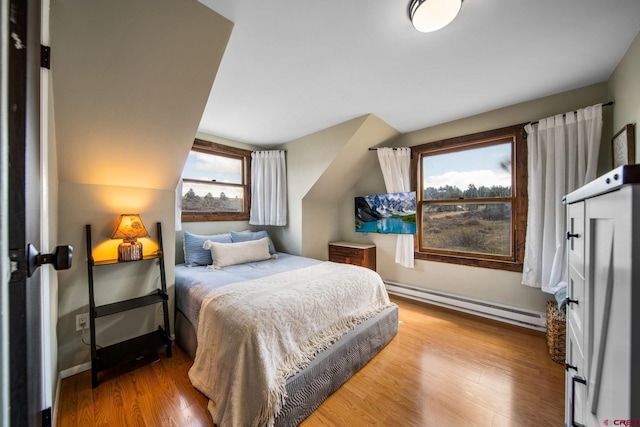 bedroom with wood finished floors, a baseboard heating unit, baseboards, and lofted ceiling