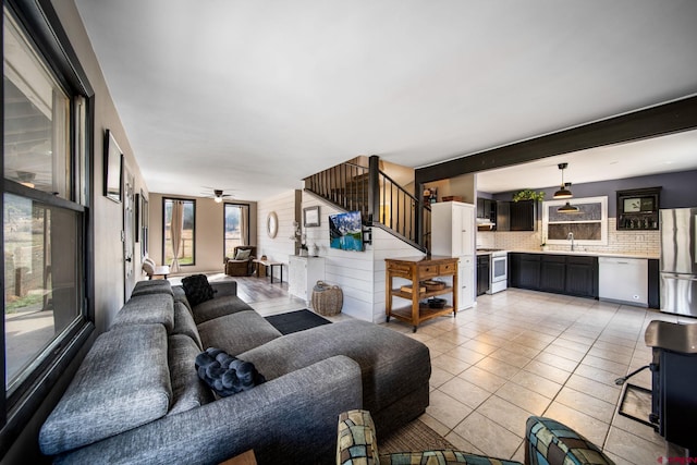 living area with light tile patterned floors, ceiling fan, and stairs