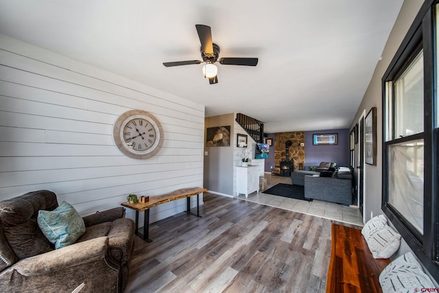 living area with wood walls, wood finished floors, ceiling fan, and a wood stove
